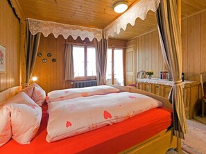 A wooden room with a bed, curtains, a radiator, and a table with a vase. - Mi Casa Appartement/Fewo, Bad, WC, 3 Schlafräume 3-Zimmerwohnung 1.Stock by Interhome (Adelboden)