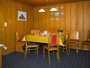Ein Esszimmer mit Holzwandverkleidung, einem für vier Personen gedeckten Tisch, Stühlen mit gepolsterten Sitzen, einem Gemälde an der Wand und einer Sammlung von Tellern.