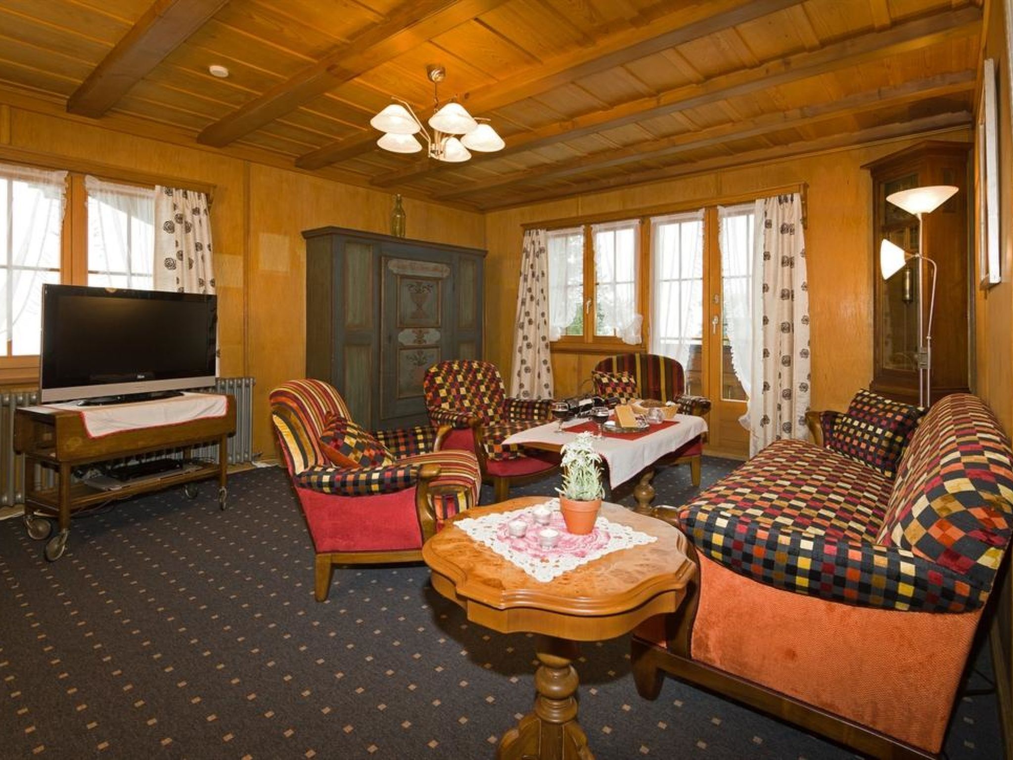 A cozy living room with a television, a dining table with chairs, a sofa, and a patterned rug.