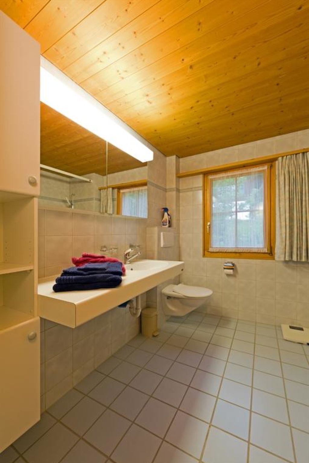 Un bagno con soffitto in legno, un lavandino bianco, un water e una finestra con tende.