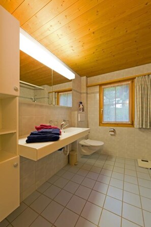 Ein Badezimmer mit Holzboden, einem weißen Waschbecken, einer Toilette und einem Fenster mit Vorhängen.