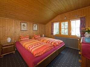 A wooden cabin room with a bed, two bedside tables, a dresser, and a window with curtains. - Mi Casa Appartement/Fewo, Bad, WC, 2 Schlafräume 2-Zimmerwohnung 2.Stock by Interhome (Adelboden)