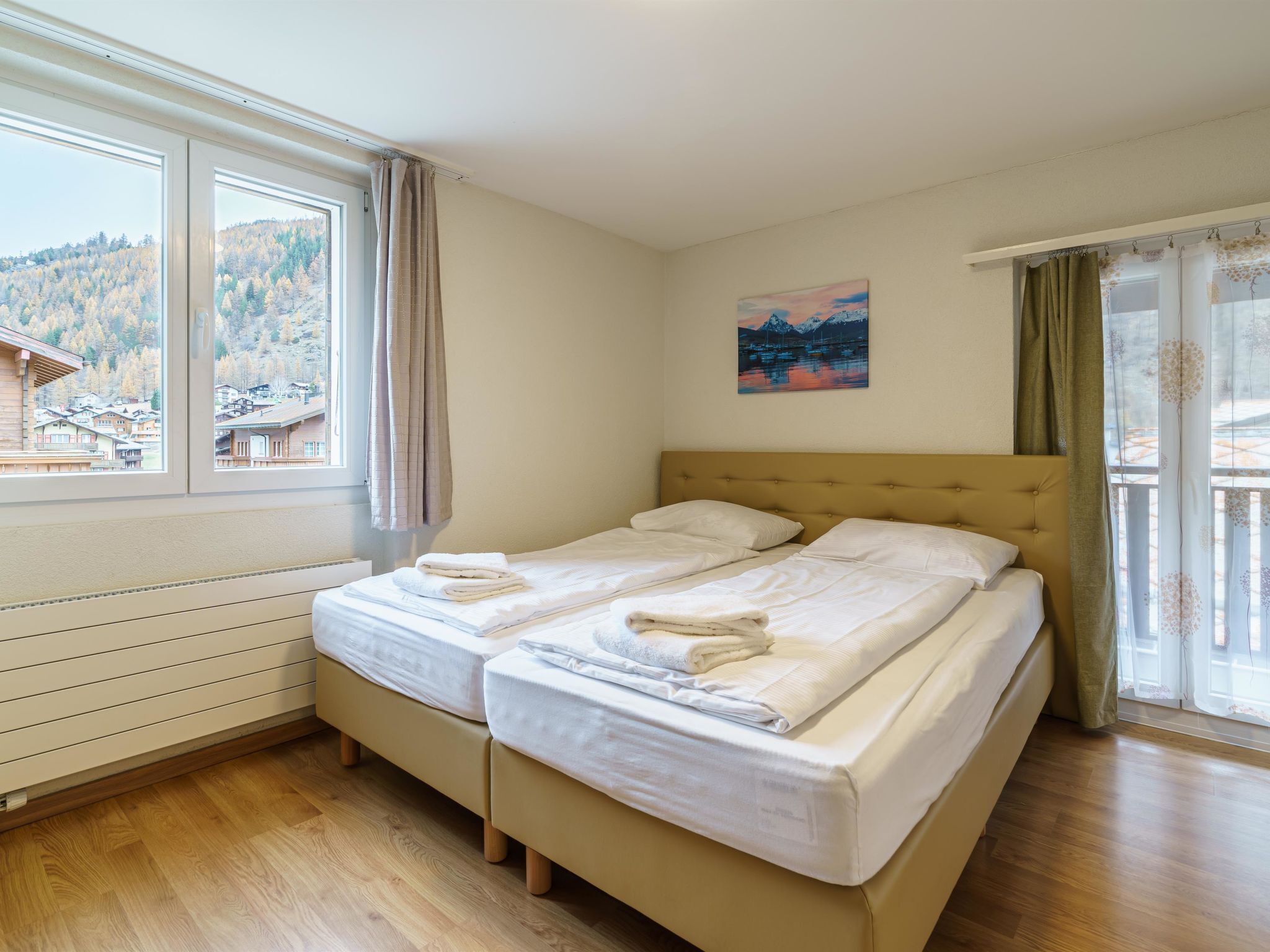 Ein Doppelbett mit weißen Leinen und Handtüchern, ein Gemälde an der Wand und Blick auf eine Berglandschaft durch das Fenster.