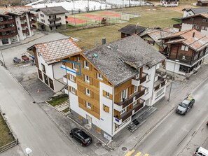 A multi-story residential building with a mix of balconies and windows, situated on a street with a sports field in the background. - Haus Astoria by Interhome (Saas-Grund)