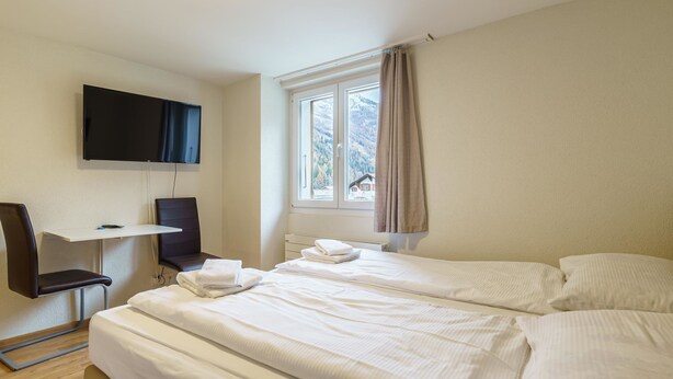 A hotel room with a bed, a desk, a chair, a TV, and a window with a view of mountains.