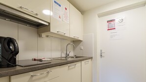 A kitchenette with a stove, sink, and cabinets. There are signs on the wall and a door with a notice.