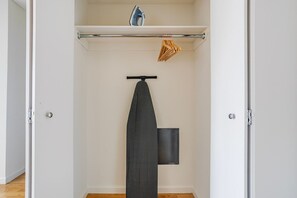 A closet with a hanging rack, an ironing board, and a shelf with a folded garment. - Blueground | East Harlem, gym, nr Central Park (New York)