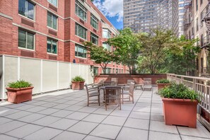 A rooftop patio with outdoor seating, potted plants, and a view of surrounding buildings. - Blueground | East Harlem, gym, nr Central Park (New York)