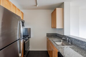 A kitchen with a stainless steel refrigerator, oven, and microwave, wooden cabinets, granite countertop, and a stainless steel sink. - Blueground | East Harlem, gym, nr Central Park (New York)