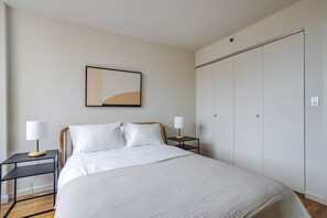 A bedroom with a bed, two bedside tables, a wall-mounted lamp, a wardrobe, and a framed picture. - Blueground | East Harlem, gym, nr Central Park (New York)