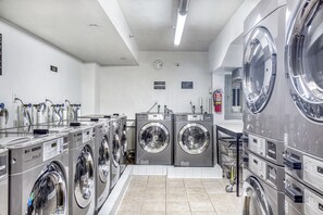 A laundry facility with multiple washing machines, a fire extinguisher, and a clock on the wall. - Blueground | East Harlem, gym, nr Central Park (New York)