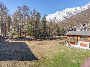 A chalet with a wooden exterior and a red door, situated in a mountainous area with snow-capped peaks in the background. - Haus Alfa by Interhome (Saas-Fee)