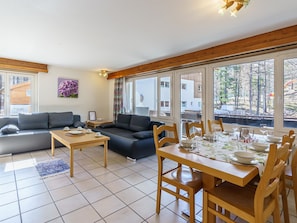 Ein modernes Wohnzimmer mit einer Couch, einem Esstisch für vier Personen und großen Fenstern mit Blick ins Freie.