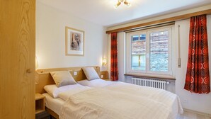 Une chambre à coucher avec un lit, une armoire en bois, un tableau encadré au mur et une fenêtre avec des rideaux.