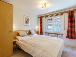 Ein Schlafzimmer mit einem Bett, einem Holzschrank, einem gerahmten Bild an der Wand und einem Fenster mit Vorhängen.