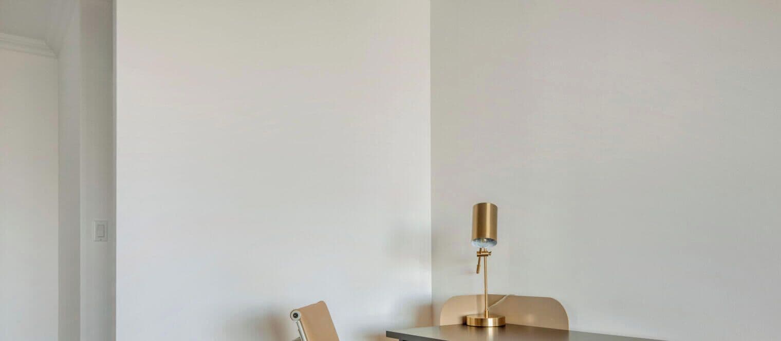 A minimalist room with a single table and a chair, a lamp, and a door.