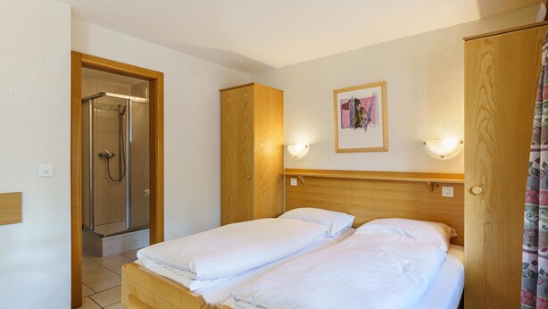 Una camera d'albergo con un letto di legno, una doccia e un quadro appeso al muro.