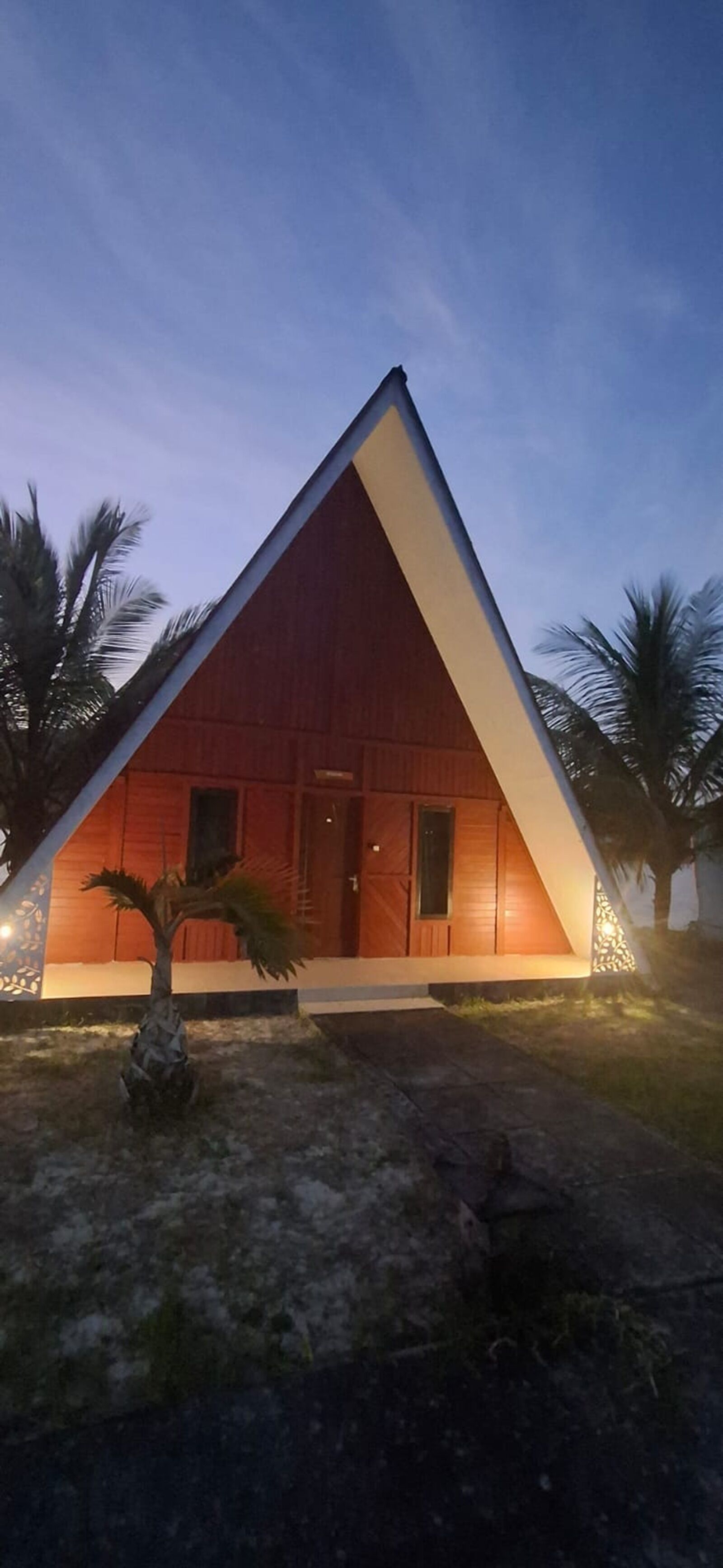 A triangular building with a flat roof, surrounded by palm trees.