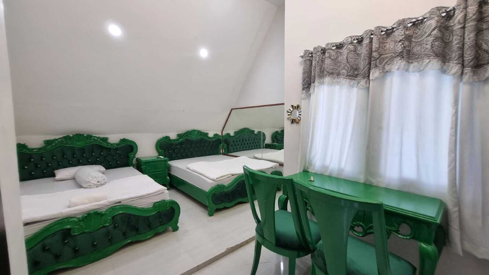 A room with two green beds, a green desk, and a chair.