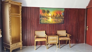 Una habitación con un armario de madera, dos sillas de mimbre y un cuadro colgado en la pared.