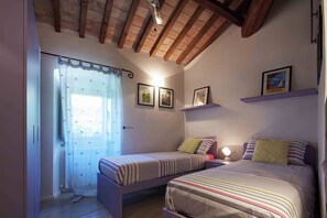 A bedroom with two beds, a window with a curtain, and wall-mounted shelves with framed pictures. - Beautiful 3-bedroom house with AC in charming Silvignano (Silvignano)
