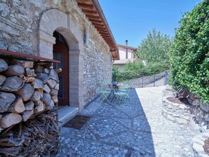 A stone building with a wooden door, a pile of firewood, a small table with chairs, and a stone wall with greenery. - Beautiful 3-bedroom house with AC in charming Silvignano (Silvignano)