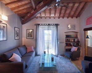 A cozy living room with a wooden ceiling, a sofa, a coffee table, a bookshelf, and a window with curtains. - Beautiful 3-bedroom house with AC in charming Silvignano (Silvignano)