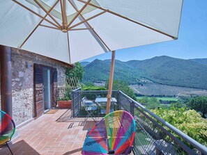 A balcony with a white umbrella, a rustic building, and a view of green hills. - Beautiful 3-bedroom house with AC in charming Silvignano (Silvignano)