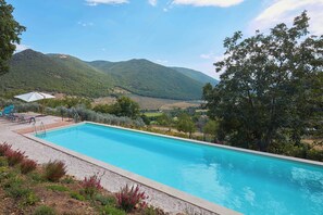 A swimming pool with a view of mountains and a garden area with chairs and umbrellas. - Beautiful 3-bedroom house with AC in charming Silvignano (Silvignano)