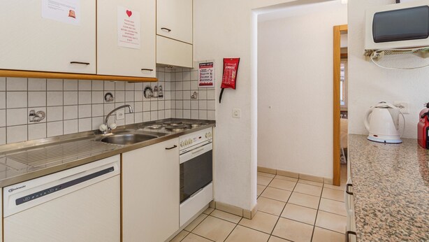 Una cocina compacta con lavavajillas incorporado, estufa y microondas. Hay letreros en la pared, incluyendo uno que solicita mantener la cocina limpia.