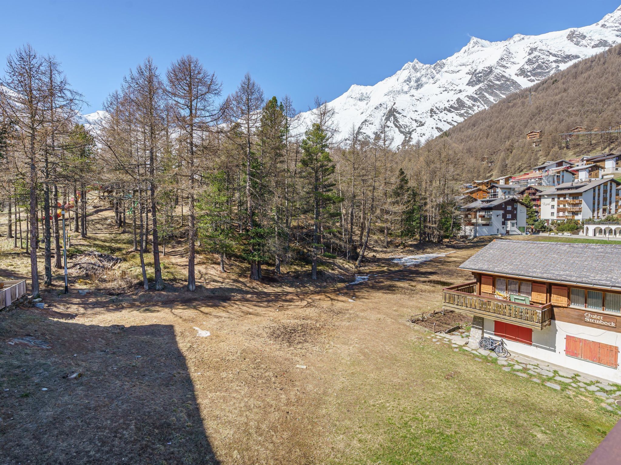 Uma pousada na montanha com vista para picos nevados, cercada por árvores e um céu claro.
