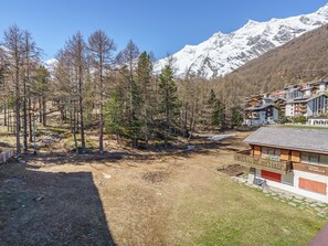 A mountain lodge with a view of snow-capped peaks, surrounded by trees and a clear sky. - Haus Alfa by Interhome (Saas-Fee)