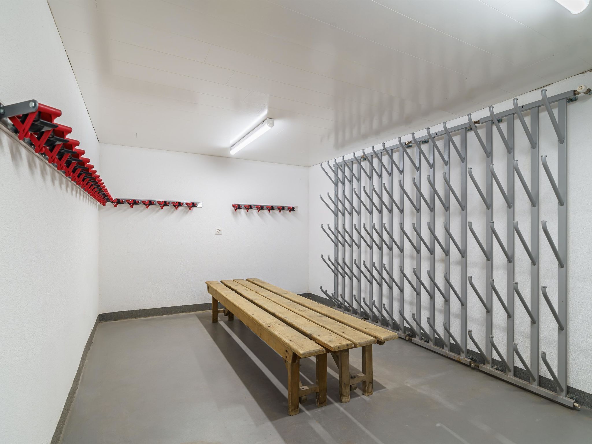 A room with a wooden bench, a red and black coat rack, and a grey metal rack with hooks.