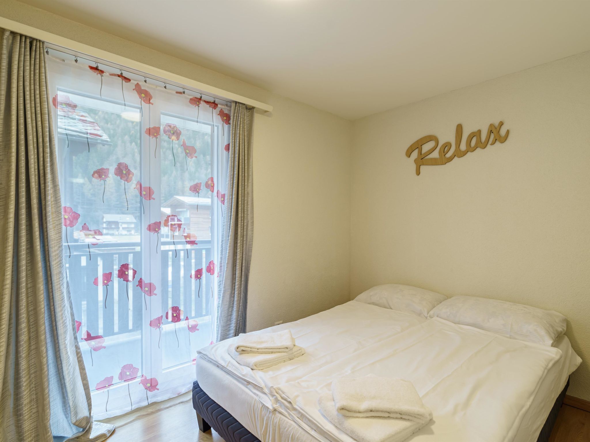 Une chambre à coucher avec un lit, une fenêtre avec des rideaux et un mur orné d’une inscription « Détendez-vous ».
