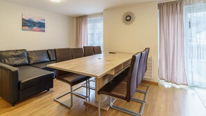 Moderni olohuone, jossa on puinen ruokapöytä, nahkasohva ja suuret ikkunat, joista avautuu näkymä ulos.