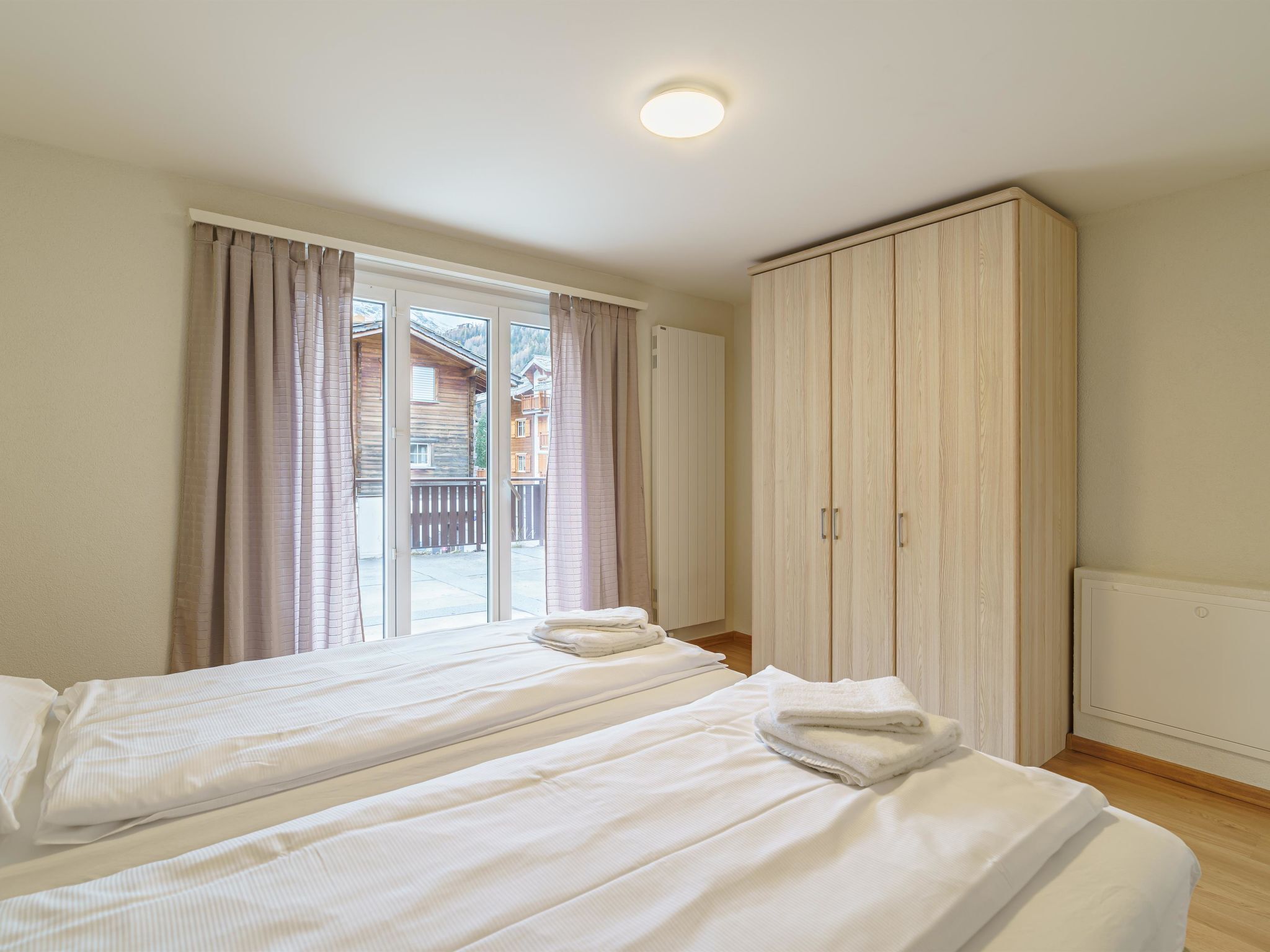 Een hotelkamer met twee bedden, een grote kledingkast en uitzicht door een glazen deur.