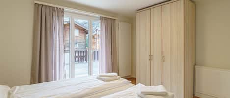 A hotel room with two beds, a large wardrobe, and a view through a glass door.