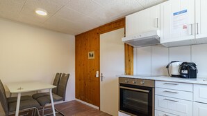 Una cocina compacta con horno integrado, armarios blancos y una puerta de madera.