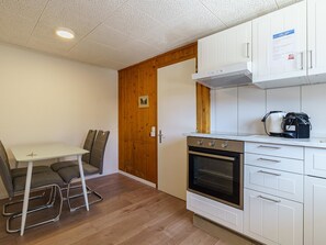 Eine kompakte Küche mit eingebautem Backofen, weißen Schränken und einer Holztür.