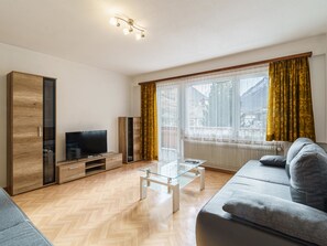 Ett modernt vardagsrum med en soffa, en tv, ett träskåp och ett soffbord i glas.
