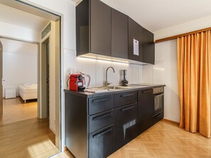A modern kitchen with black cabinetry, a built-in oven, and a coffee maker. - Haus City by Interhome (Saas-Grund)