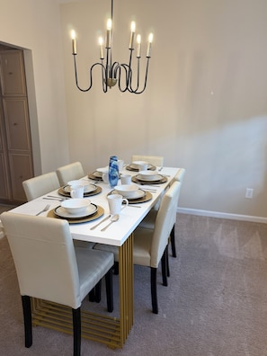 A dining room with a chandelier, white table, and chairs.
