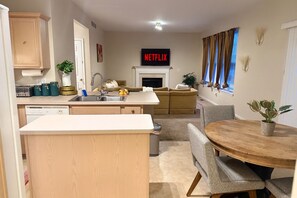 Una cocina moderna con lavavajillas integrado, comedor con mesa y sillas de madera, sofá y chimenea.
