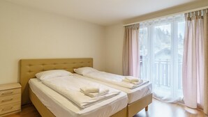 Et hotelværelse med to senge, en trækommode og et stort vindue med gardiner.