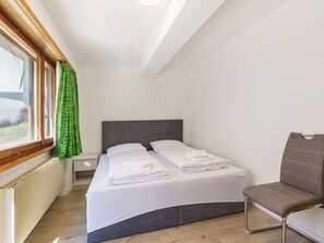 A hotel room with a bed, a chair, a window with curtains, and a radiator. - Haus Slalom by Interhome (Saas-Fee)