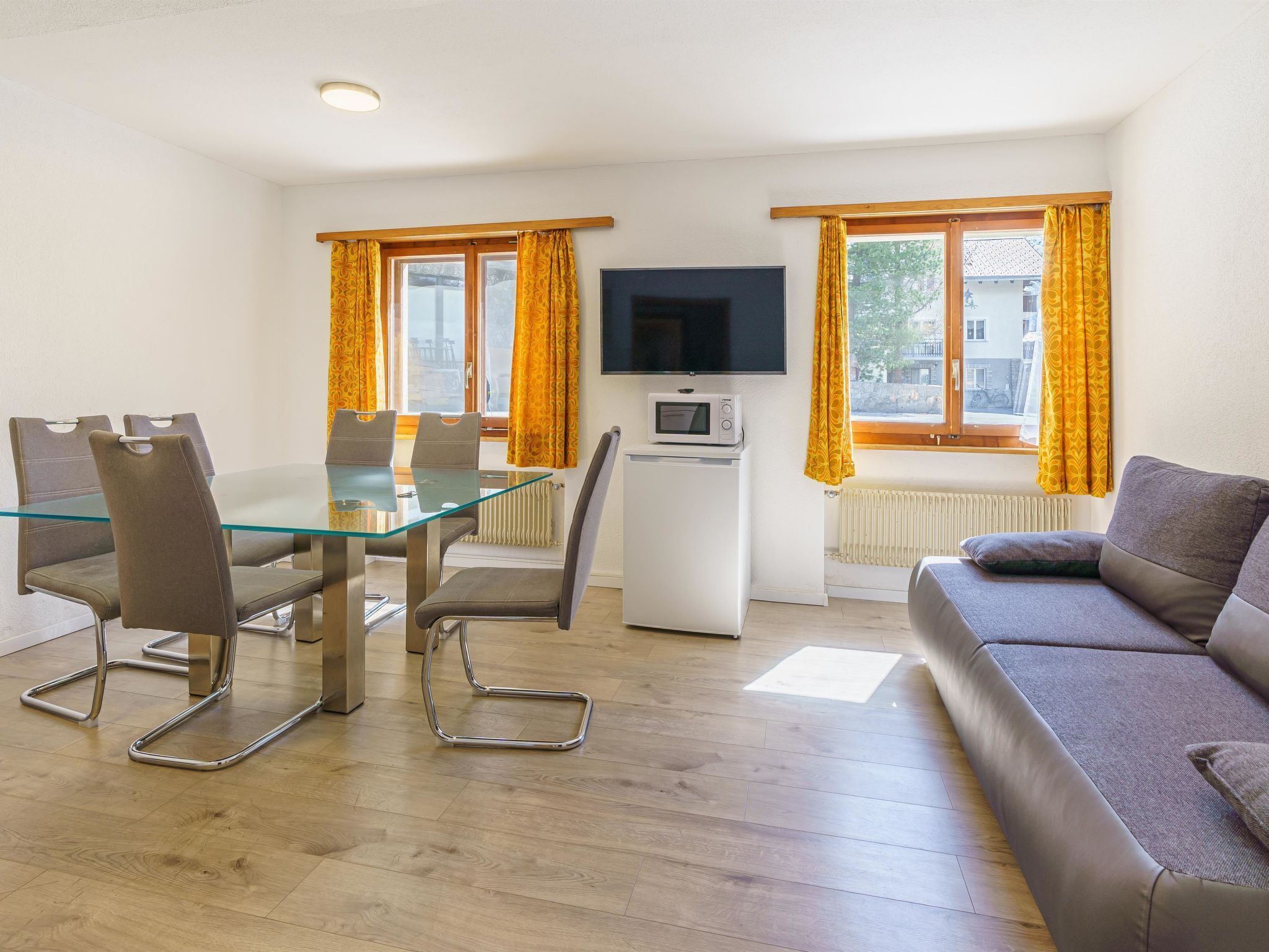 Een moderne woonkamer met een glazen eettafel, twee stoelen, een bank, een flatscreen televisie en een magnetron.