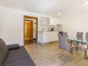 A modern kitchen with white cabinets, a dining table with chairs, and a wooden door leading to another room. - Haus Slalom by Interhome (Saas-Fee)