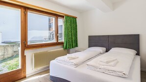 A bedroom with a large window, a radiator, and a bed with neatly folded towels. - Haus Slalom by Interhome (Saas-Fee)
