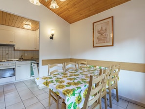 A dining area with a table set for four, wooden chairs, a kitchen in the background, and a framed picture on the wall. - Haus Alfa by Interhome (Saas-Fee)