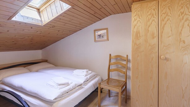 Ein Schlafzimmer mit einem Bett, einem Holzstuhl, einem Kleiderschrank und einem Dachfenster.